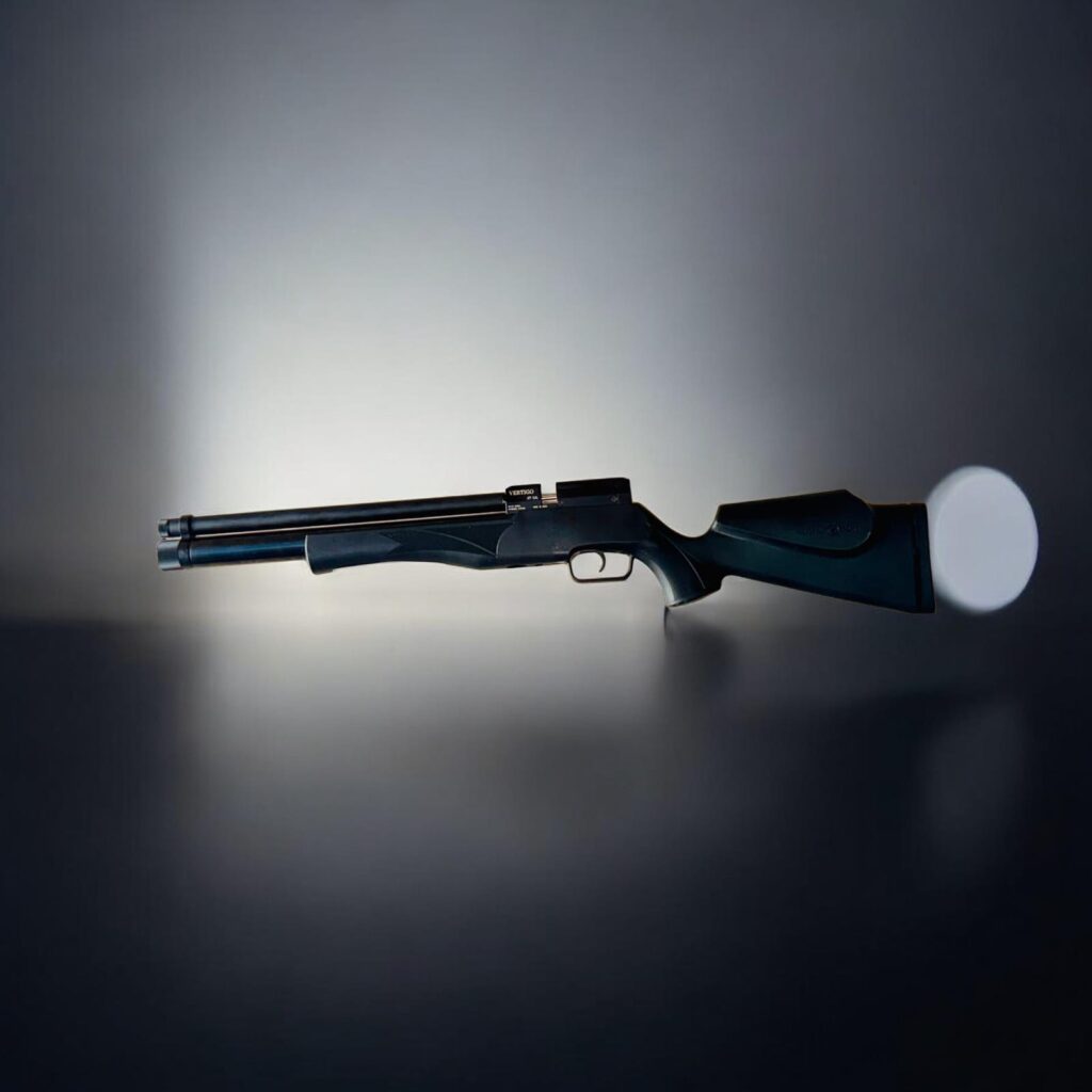 Side view of a double-barrel shotgun resting on a reflective surface against a dark gradient background, handgun-style stock visible.