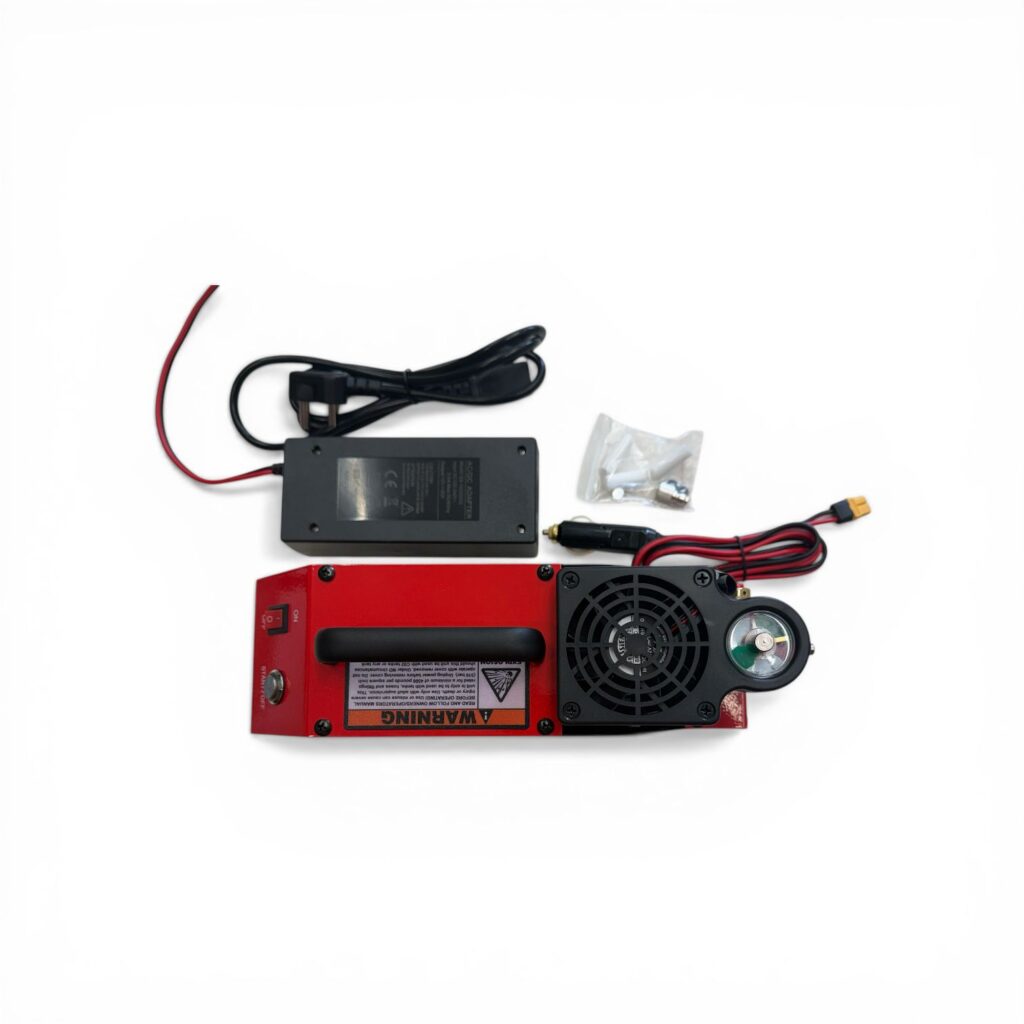 Red electronic device with a built-in cooling fan and warning label, connected to a black power brick and red/black cables with a small bag of screws nearby.